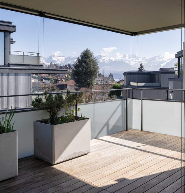 Terrasse mit Holzboden und Windschutz aus Glas, mit Blick auf die Alpen in Hünibach