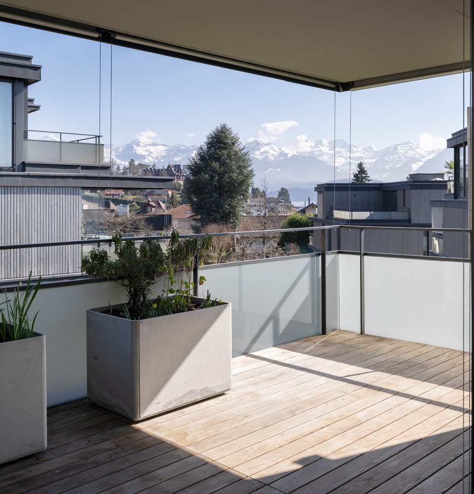 Terrasse mit Holzboden und Windschutz aus Glas, mit Blick auf die Alpen in Hünibach